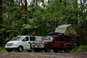 Two SUVs with camping gear in a lush forest, ideal for travel and adventure enthusiasts.